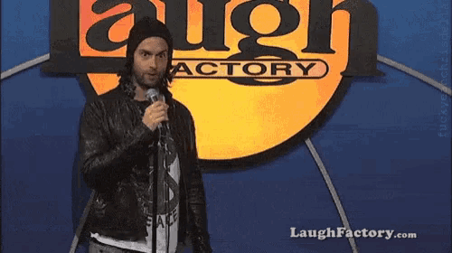 a man stands in front of a laugh factory sign holding a microphone