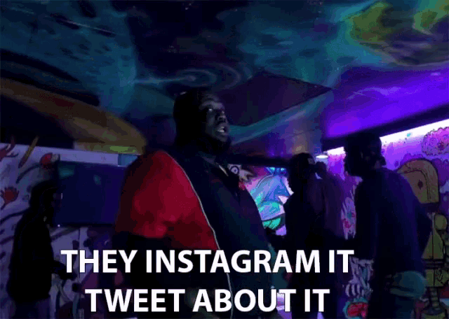 a man in a red and black jacket is standing in a dark room and says they instagram it tweet about it
