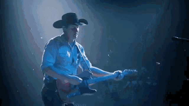 a man in a cowboy hat is playing a guitar in front of a microphone