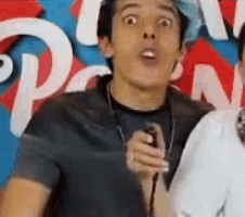 a young man with blue hair is holding a microphone and making a funny face in front of a pizza hut sign .