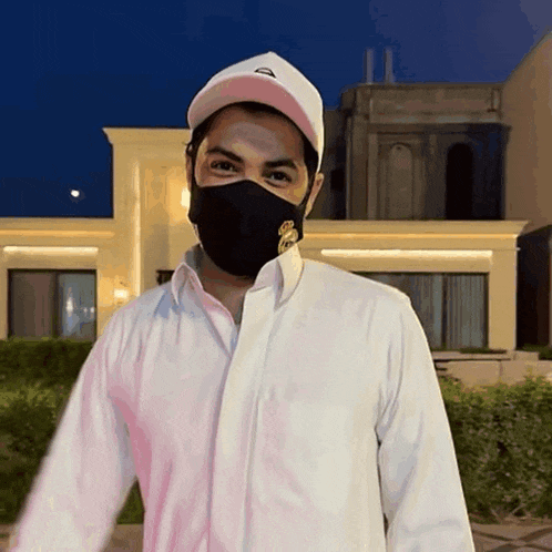 a man wearing a white shirt and a black mask is standing in front of a building
