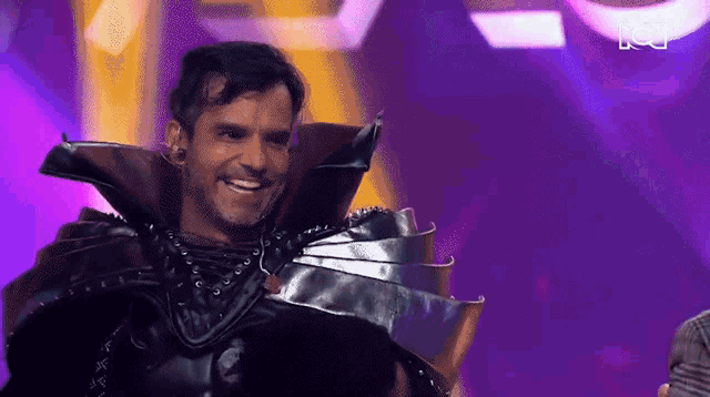a man in a black costume is smiling on a stage in front of a purple background