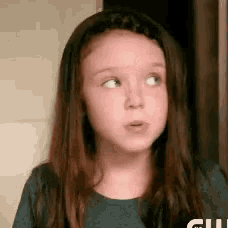 a young girl with long brown hair is wearing a blue shirt and looking up .