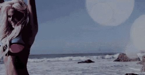 a woman in a bikini is standing on the beach looking at the ocean .