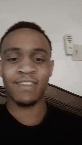 a man in a black shirt is smiling with a remote control hanging on the wall behind him