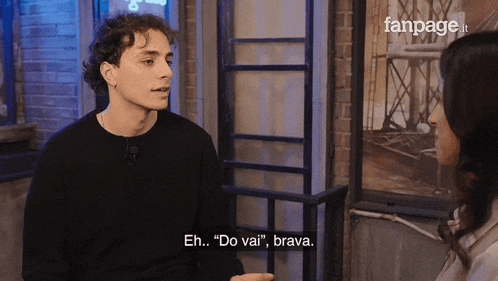 a man in a black sweater is talking to a woman in a fanpage video
