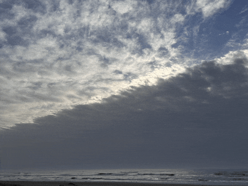 a cloudy sky over the ocean with the sun shining through it