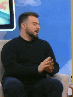 a man with a beard is sitting in a chair talking