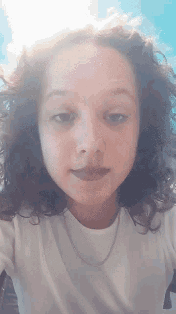 a young girl with curly hair is wearing a white shirt and a chain around her neck
