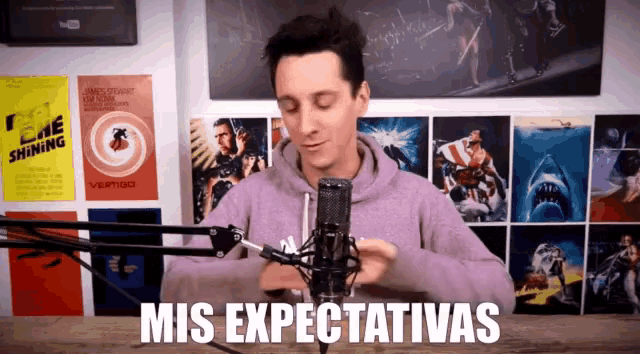 a man in a purple hoodie stands in front of a microphone with the words mis expectativas written below him