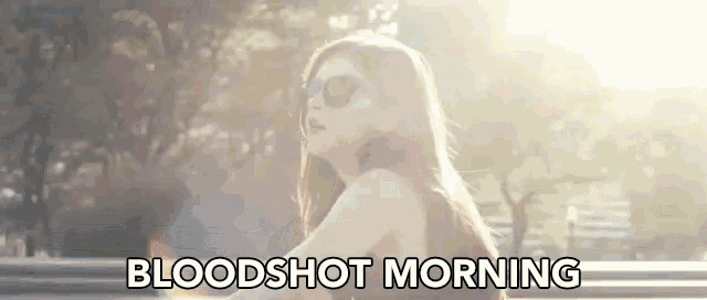 a woman wearing sunglasses is standing in the sun with the words bloodshot morning above her .