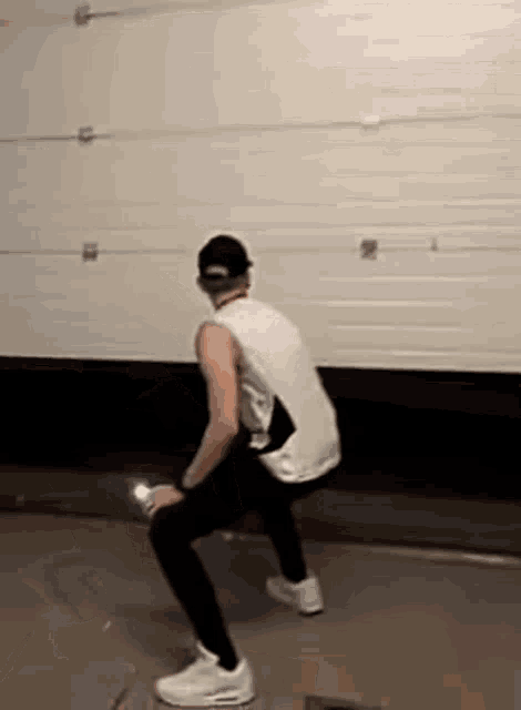 a man is squatting in front of a garage door in a garage .