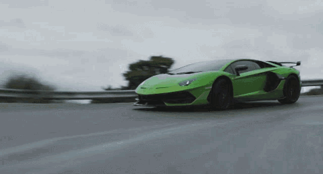 a green sports car is driving down a road with trees in the background