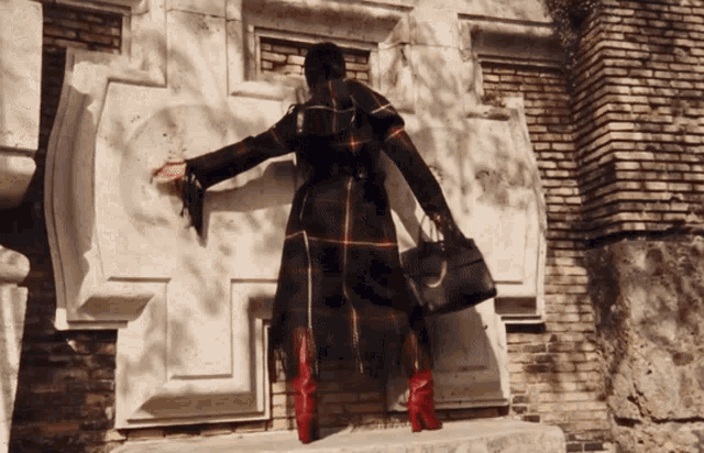 a woman in a plaid coat and red boots is standing in front of a brick building
