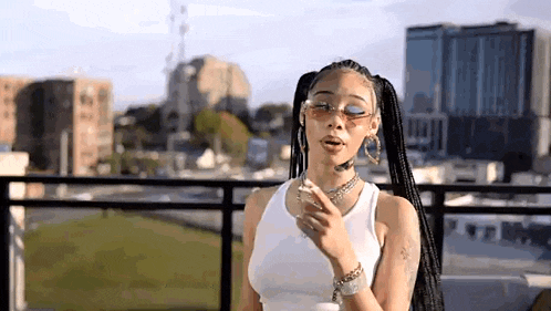 a woman wearing a white tank top and sunglasses is standing on a balcony .