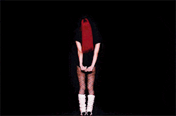 a woman with red hair is standing in the dark with her hands behind her back .