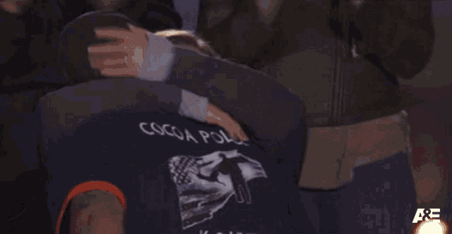 a man in a cocoa police shirt hugging another man