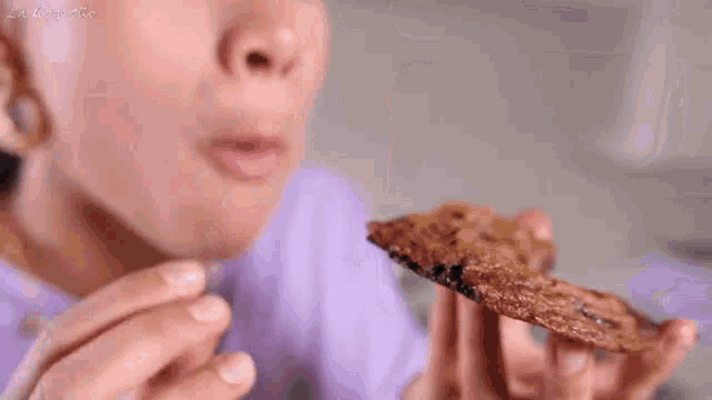 a woman in a purple shirt is eating a cookie with la doguette written on the bottom right