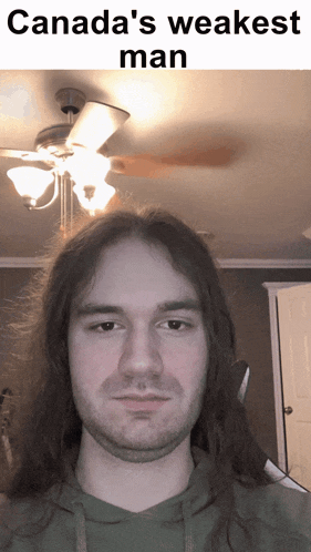 a man with long hair and a beard stands in front of a ceiling fan