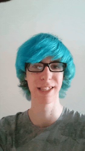 a boy with blue hair and glasses is smiling for the camera