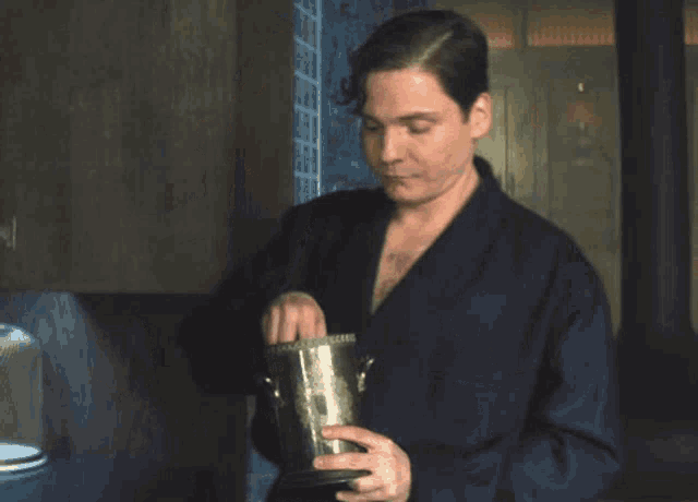 a man in a blue robe is holding a silver bucket in his hands