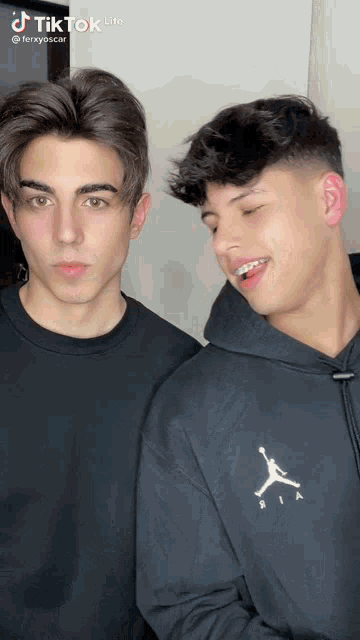 two young men are standing next to each other and one of them is wearing a black hoodie with a jordan logo on the front .