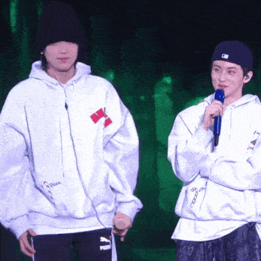 a man holding a microphone stands next to another man wearing a hoodie that says puma on it