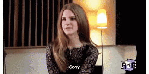 a woman with long hair is sitting in front of a lamp and saying sorry .