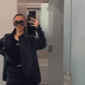 a woman wearing sunglasses is taking a picture of herself in the mirror