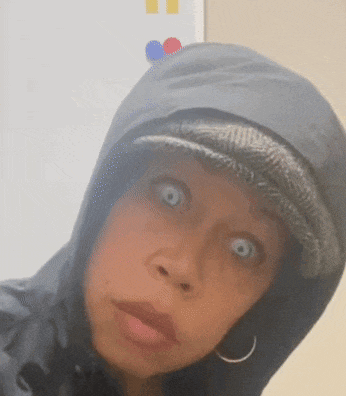 a woman wearing a hooded jacket and a hat has a surprised look on her face