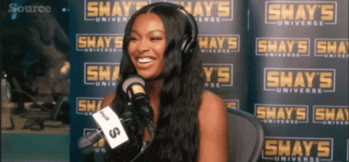 a woman is smiling in front of a shay 's universe sign