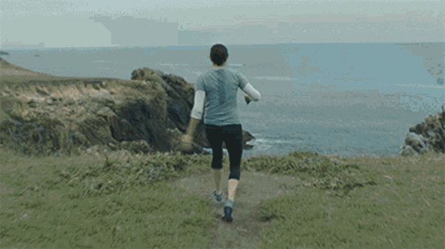 a woman is running on a grassy hill near the ocean