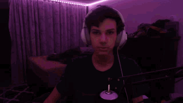 a man wearing headphones is taking a selfie in a dark room with purple lights behind him .