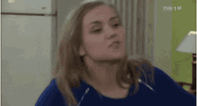a woman in a blue shirt is making a funny face while standing in a living room .