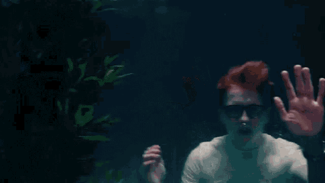 a man with red hair and glasses is swimming underwater and waving at the camera .