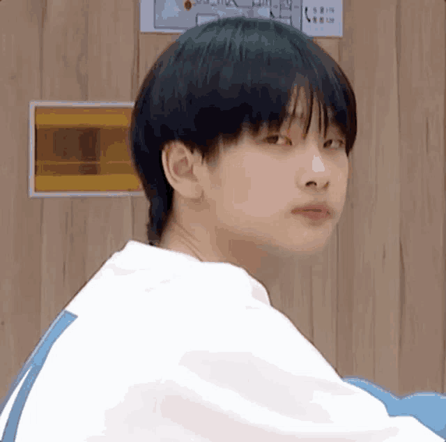 a young boy with black hair is sitting in front of a wooden wall .