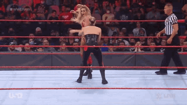 two women are wrestling in a wrestling ring while a referee looks on .
