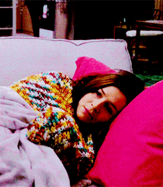 a woman laying on a couch with a pink pillow and a blanket