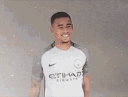 a man wearing a white and gray etihad airways shirt is smiling .