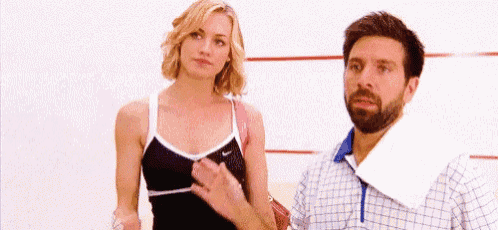 a man and a woman are standing next to each other on a squash court . the woman is wearing a sports bra .