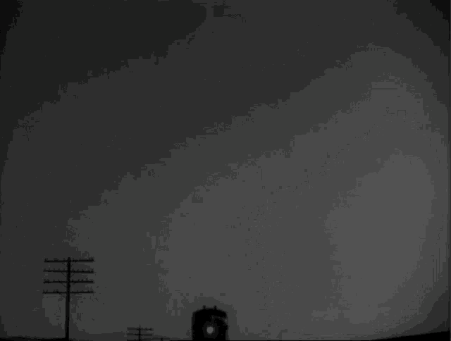 a black and white photo of a train in the dark with telephone poles in the background