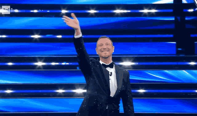 a man in a tuxedo is standing on a stage with his hand up