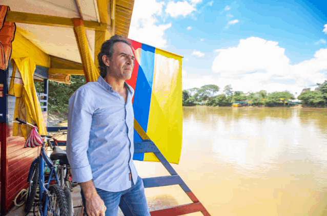 a man in a blue shirt stands in front of a bicycle and a flag