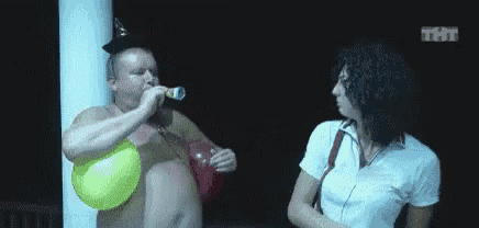 a shirtless man is blowing up a yellow balloon while a woman looks on .