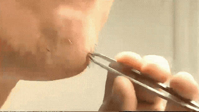 a close up of a person using tweezers to remove a bug from their nose