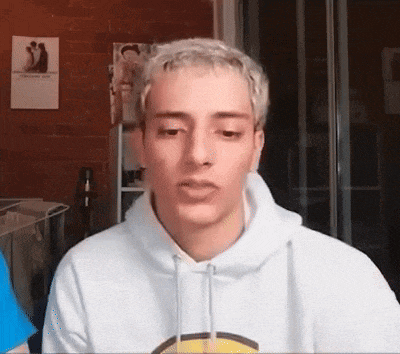 a young man with blonde hair is wearing a white hoodie and looking at the camera .