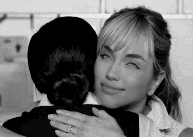 a black and white photo of two women hugging each other in a room .