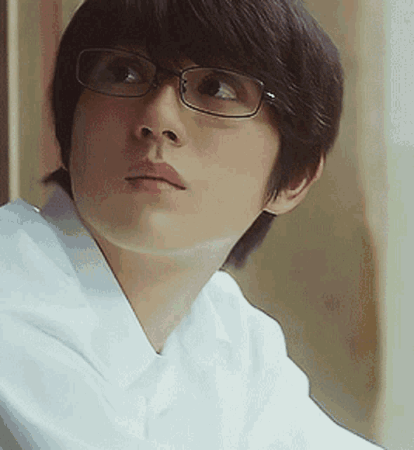 a young man wearing glasses and a white shirt is looking at the camera