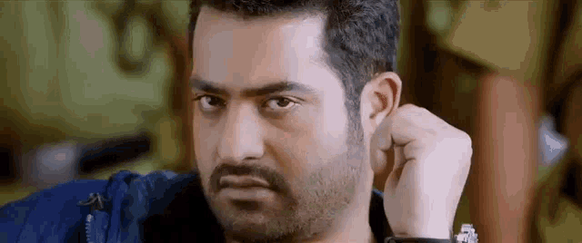 a man with a beard is holding his fist to his ear and looking at the camera .