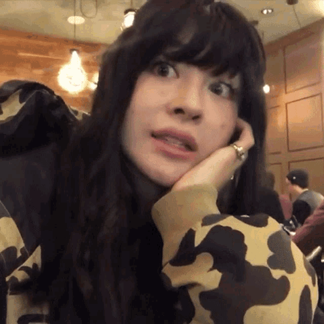 a woman wearing a camouflage jacket looks at the camera